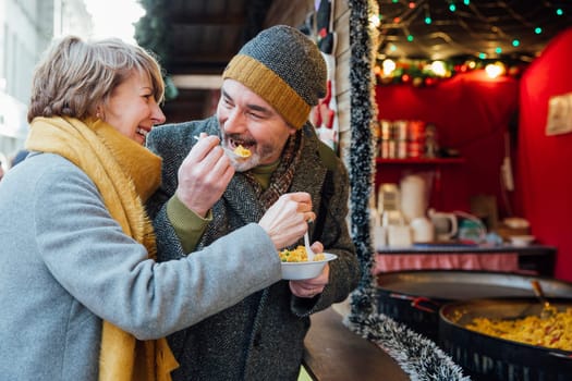 Mature couple are enjoying sharing some paella from a christmas market stall