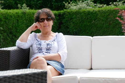 portrait of  smiling middle age woman with sunglasses  sitting in garden at home