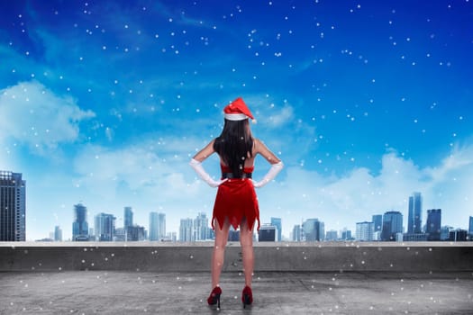 Asian woman wearing santa claus costume, standing on the rooftop, looking the city