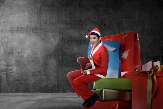 Young asian man wearing santa claus costume sit on the big present box