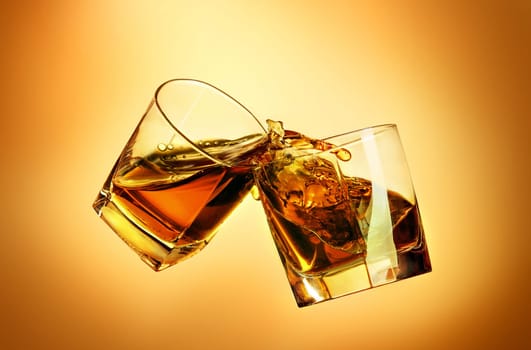 Two whiskey glasses clinking together on brown studio background