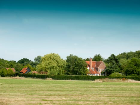 country farm house behind trees and field  Essex  UK