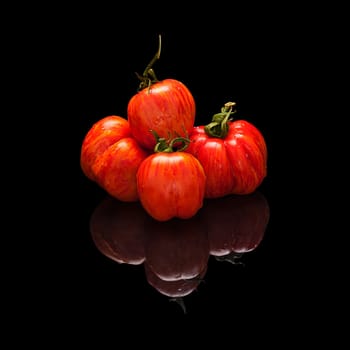 Pile tomato red-orange isolated on black glossy background with real reflection