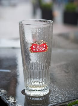 ANTWERP, BELGIUM - OCTOBER 2, 2016: Empty glass of Stella Artois beer on a rainy wet table. It is a pilsner brewed in Leuven Belgium since 1926