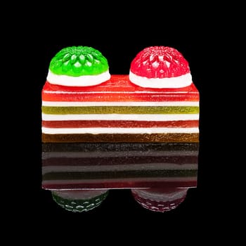 Rectangular piece of colored marmalade isolated on black glossy background with real reflection. Side view.
