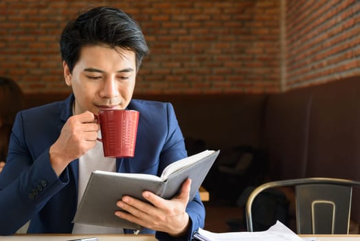 young asian businessman working while drinking red cup coffee in the office