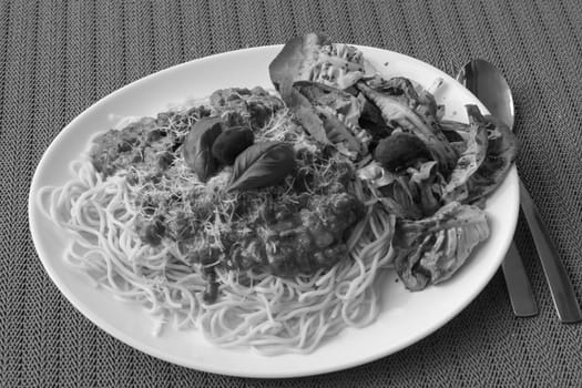 Spaghetti Bolognese with basil leaf,salad and red Spanish olives. Black and white image..