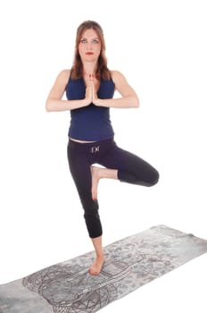 A slim young woman in an exercising outfit standing on a gray towel.on one leg with her hands folded, isolated for white background.