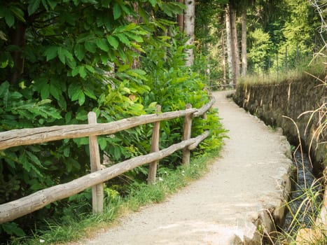 Idyllic hiking trail with railings and small irrigation flow through a forest above the city of Merano in South Tyrol.