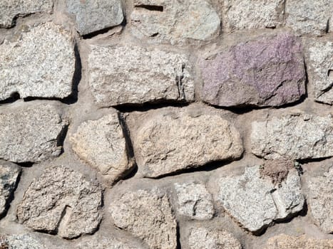Format-filling view of irregular granite stones as a masonry wall with joints.