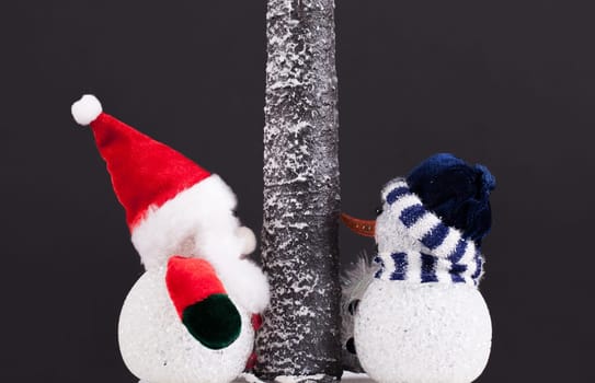Toy Father Christmas and snowman under a tree. Festive scene on a black background
