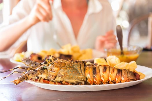 Lady on tropical vacations eating grilled lobster served with potatoes and coconut sauce.