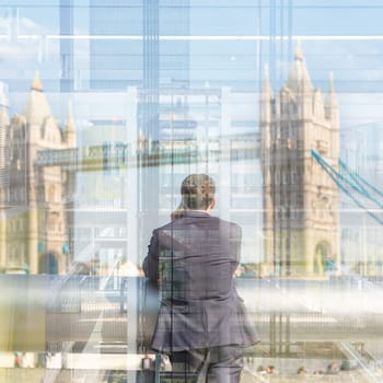 Businessman talking on mobile phone while looking trought the business office window at Tower Bridge in London city, UK.