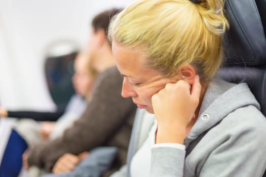 Tired blonde casual caucasian lady napping on seat while traveling by airplane. Commercial transportation by planes.