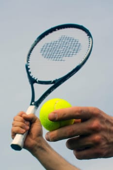 Male hands are holding a tennis ball and racket.