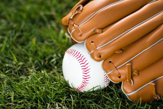 Baseball glove and ball are on green grass background.