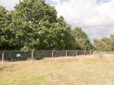 a wire fence protecting a fishing lake from otters outside in summer field  Essex  UK