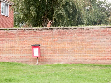 a red dog poo box bin outside against wall no people  Essex  UK