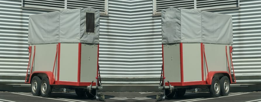 Old horse transport trailer in front of a metal wall..