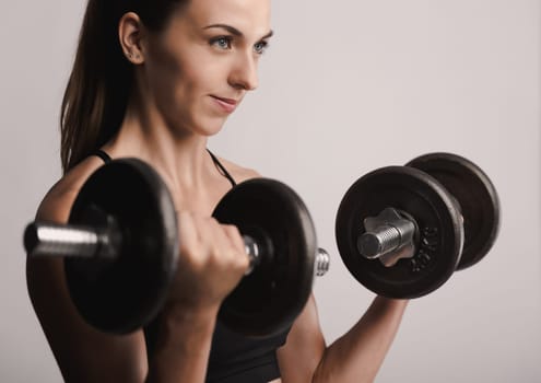 Beautiful young woman in a workout gear lifting dumbbells