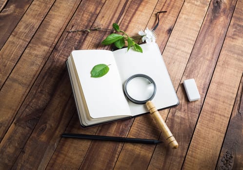 Blank notepad, magnifier, pencil, eraser, cherry flowers and green leaves on wooden background. Stationery elements. Responsive design mockup.
