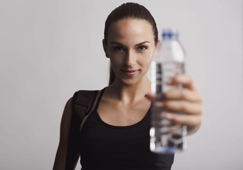 Portrait of sporty young woman holding a water bottle, against a gray background
