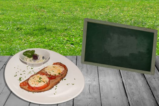 Slice of bread with tomato gratinated with cheese on a wooden table. In the background meadow and a table..