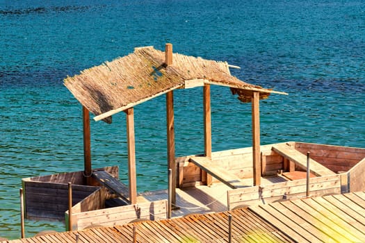 Jetty with simple boathouse or wooden boat with thatched roof..