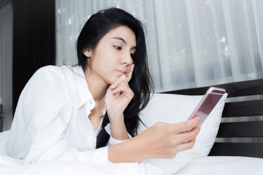 Young Asian woman playing puppy doll on the bed in morning bedroom, alone and lonely
