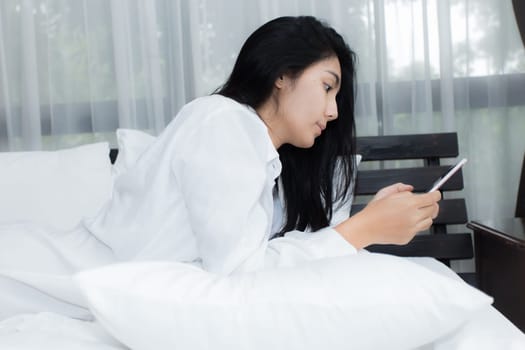 Young Asian woman playing puppy doll on the bed in morning bedroom, alone and lonely