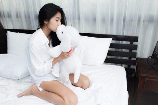 Young Asian woman playing puppy doll on the bed in morning bedroom, alone and lonely