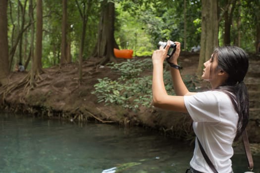 Young asian woman taking photos in autumn forest with camera