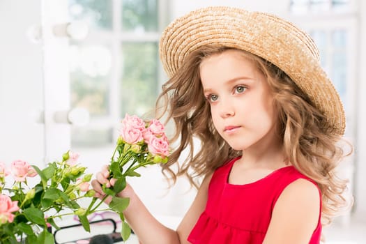 A little girl with red dress and cosmetics. She is in mother's bedroom, sitting near the mirror.