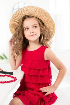 A little girl with red dress and cosmetics. She is in mother's bedroom, sitting near the mirror.