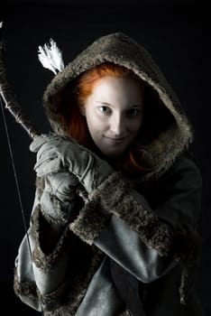girl archer in a costume with bow isolated in a dark background