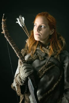 girl archer in a costume with bow isolated in a dark background