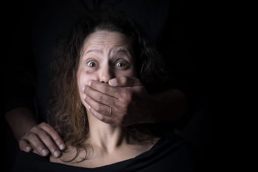 Scared woman with man's hand covering her mouth, victim of domestic violence