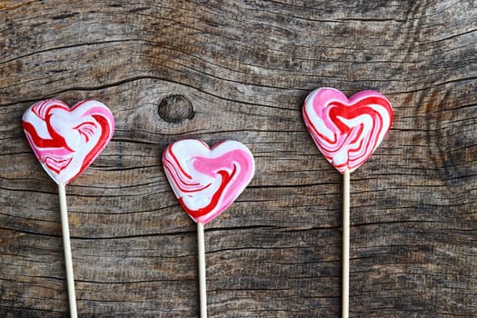 Three white-red lollipops in heart shape on a wooden background
