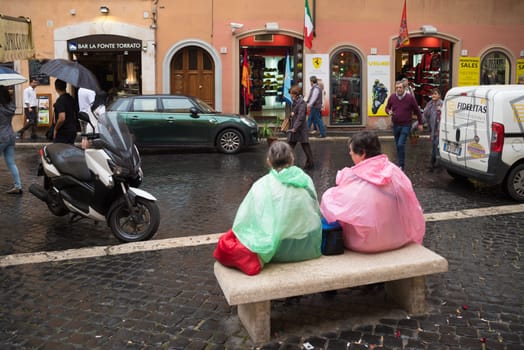 ROME, ITALY - OCTOBER 18, 2016: Two unknown tourists with colorful rain coats sitting on a bench