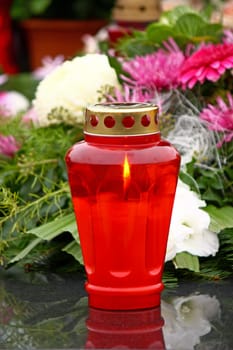 Illuminated votive candle glows on a grave, lantern