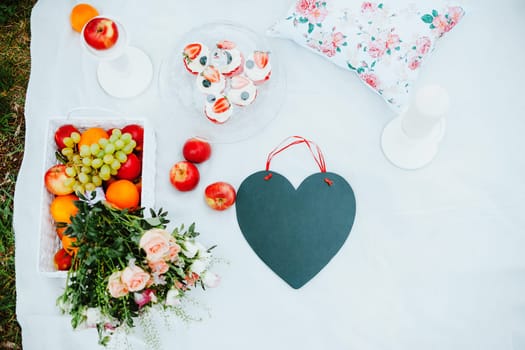 Picnic on the glade for lovers, with fruit and cakes, black chalkboard in the form of a heart, a love story