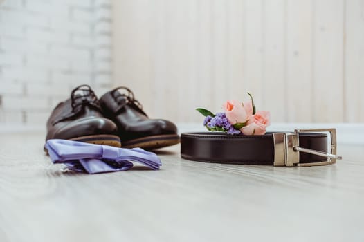 Boutonniere of the groom of a rose, a blue bow tie, brown shoes and a belt for the groom
