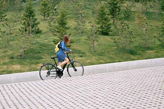 A young girl in zhdinsovom sarafan, on a bicycle, climbs uphill. Bike tours in the city