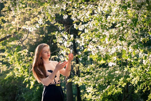 A girl in the garden, holding a branch with apple blossoms in her hands. In the apple orchard. Spring abstract, apple blossom