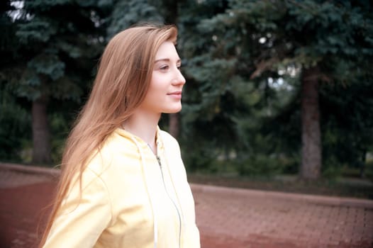 A pretty girl with long red hair, walks through the park and smiles. Portrait in the open air