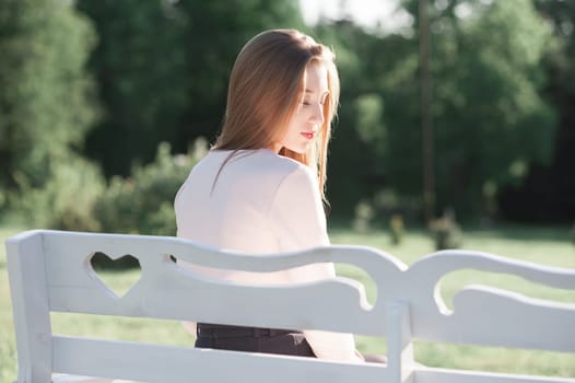 Cute young girl sitting on a white bench. The girl is sad. Portrait of an outdoor lifestyle.