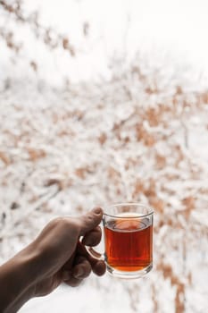 Transparent mug with tea. Hand holding a cup of tea. A mug of tea is hanging in the air. In the morning the composition creates a good mood.