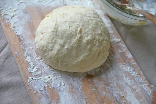 Ball of dough on a cutting board with napkin and mixing bowl