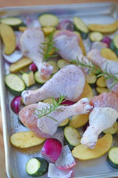 Baking sheet with chicken legs, zucchini, rosemary, onions, and potatoes before going in the oven