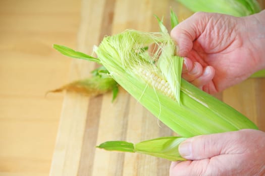 A man pulls the husk from an ear of corn over a cutting board